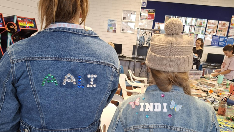 Two young ladies with their backs to the camera wearing denim jackets that they have decorated.