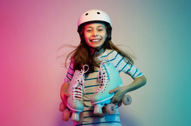Young girl wearing a helmet and holding a pair of roller skates
