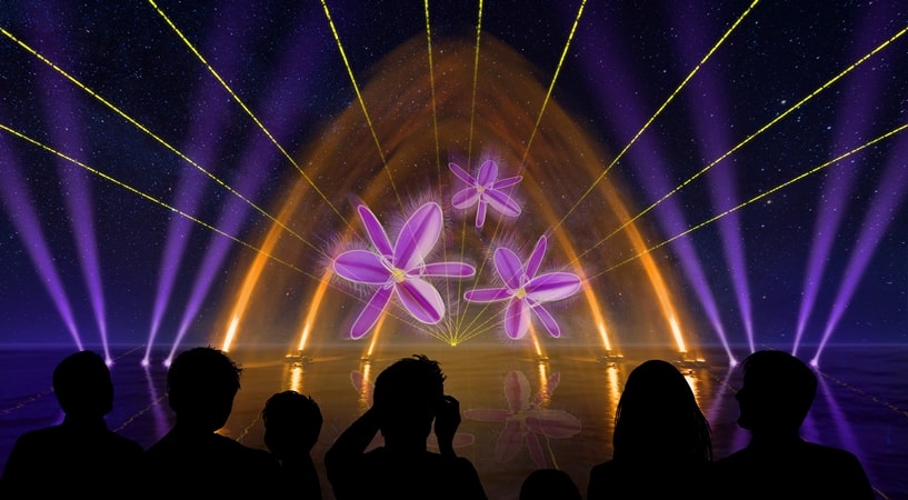 An artist's impression of laser lights and projections of flowers over the water with silhouettes of people watching.