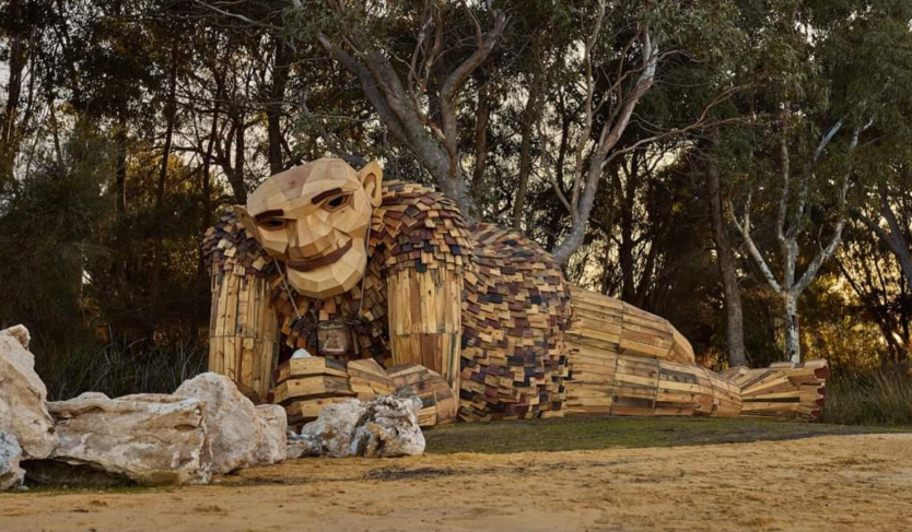 A wooden sculpture of a giant lies on its stomach among the trees