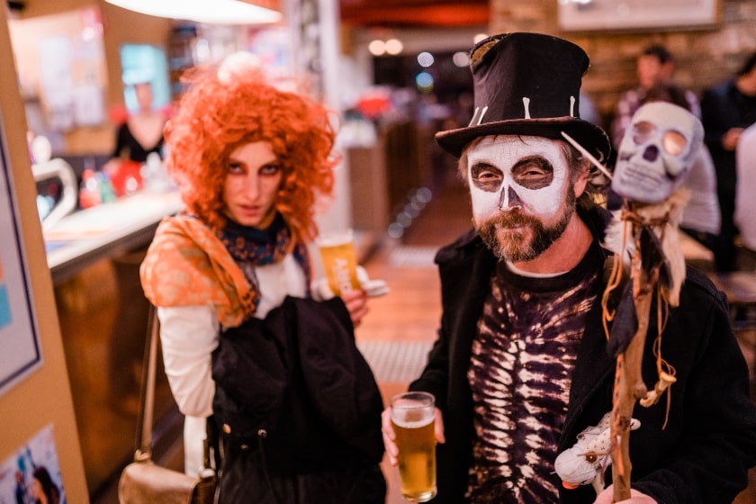 Man and woman dressed in Halloween costumes. Man as a skeleton with a top hat. The woman with an orange curly wig.