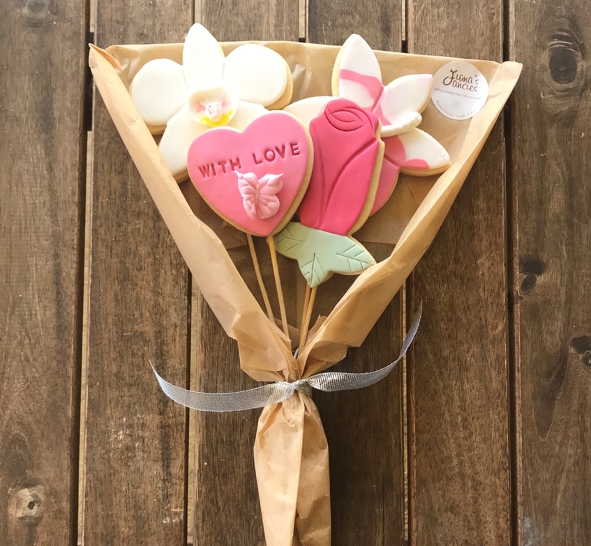 Cookies decorated as flowers in a bouquet, wrapped with brown paper and a white ribbon.