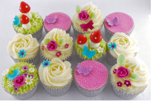 A dozen cupcakes with white, pink, green, red and blue decorations to look like a garden and flower scene.