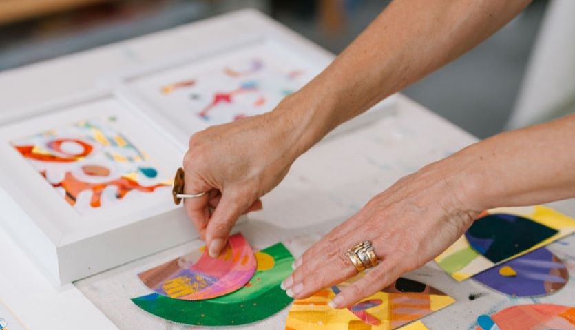 A pair of hands places arranges pieces of coloured paper into a collage effect