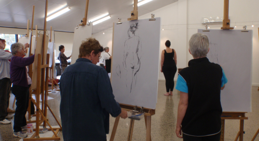 a group of people are standing at their own easels, drawing a sketch of a woman wearing a black singlet and leggings