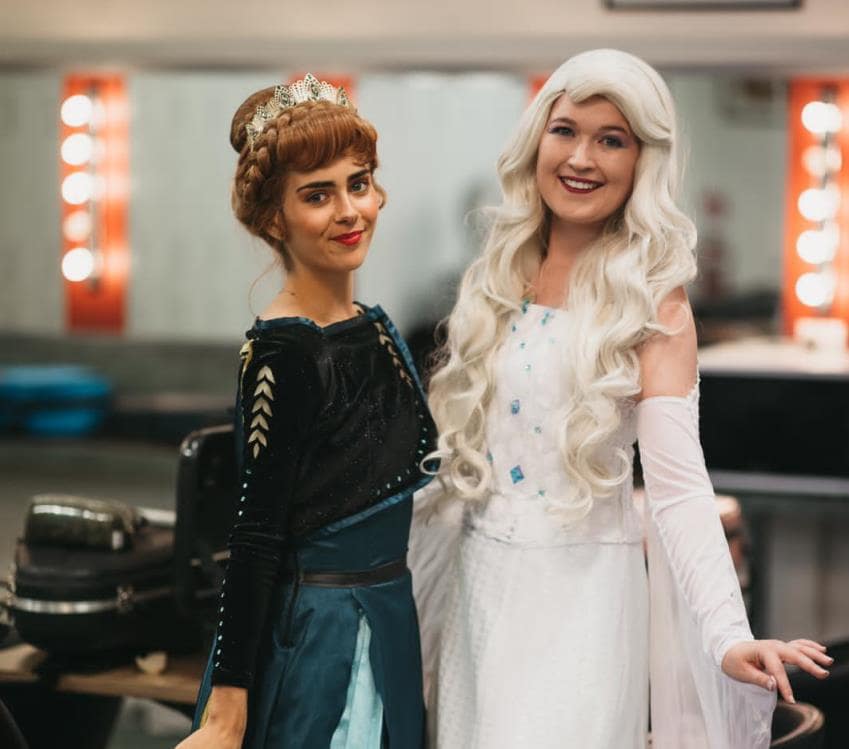 Two princesses standing side by side, smiling. One dressed in white the other green.