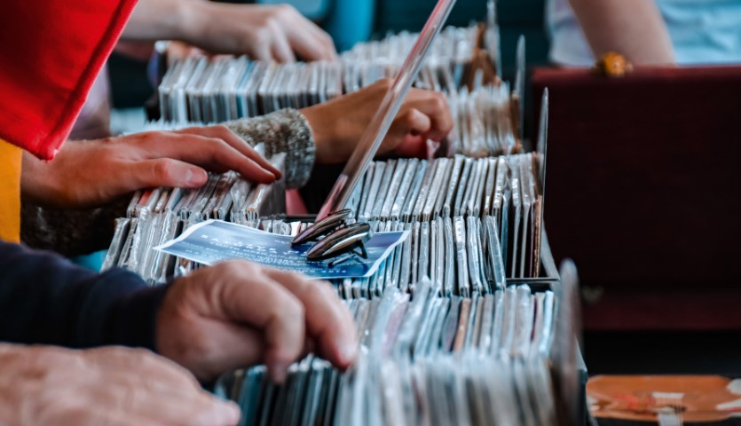 Boxes of vinyl records sit in a row, while various hands flick through and look at the covers