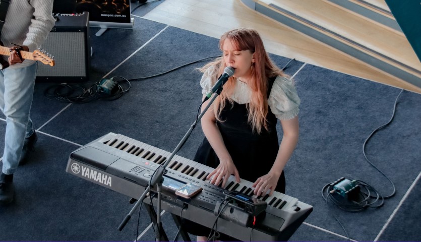 A young woman sits at a keyboard, playing and singing into a microphone
