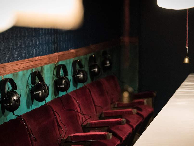 A line of red velvet cinema style chairs with headphones handing behind them