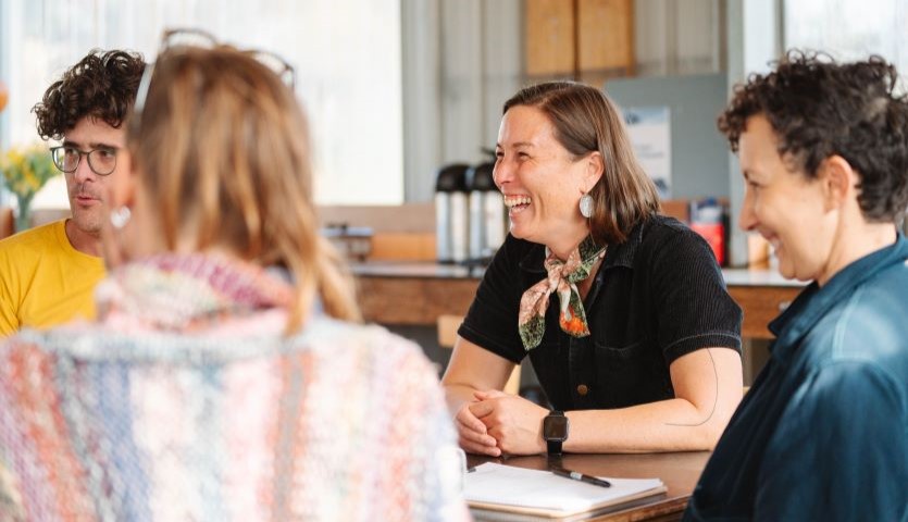Four people sit around a table in a conference room, smiling and talking