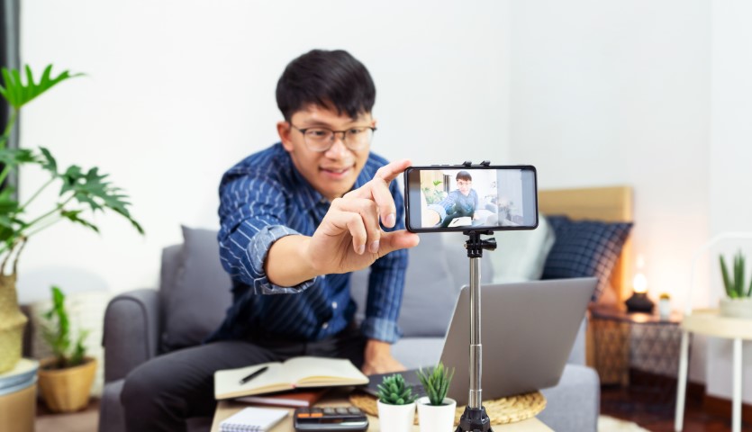 A man sits on a couch and points his camera at himself ready to take a video
