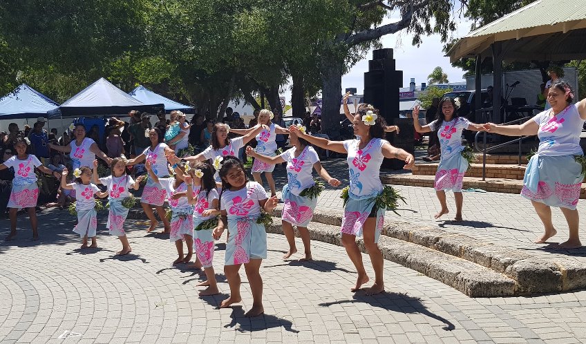Traditional New Zealand dance being performed outside by a group of girls and women wearing pink and blue costumes.
