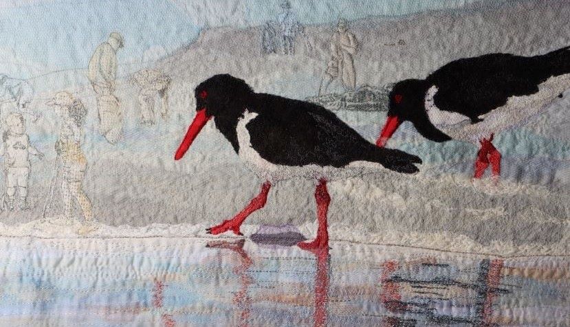 Textile art depicting two black and white birds in a coastal setting