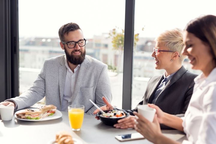 Three people sitting at table with orange juice and bowls in front of them.