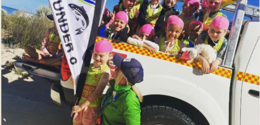 Group of children on back of ute at beach wearing bring pink swimming caps.