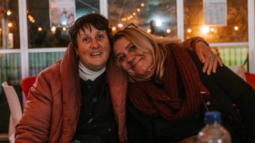 Two women sitting, one with her arm around the other. 