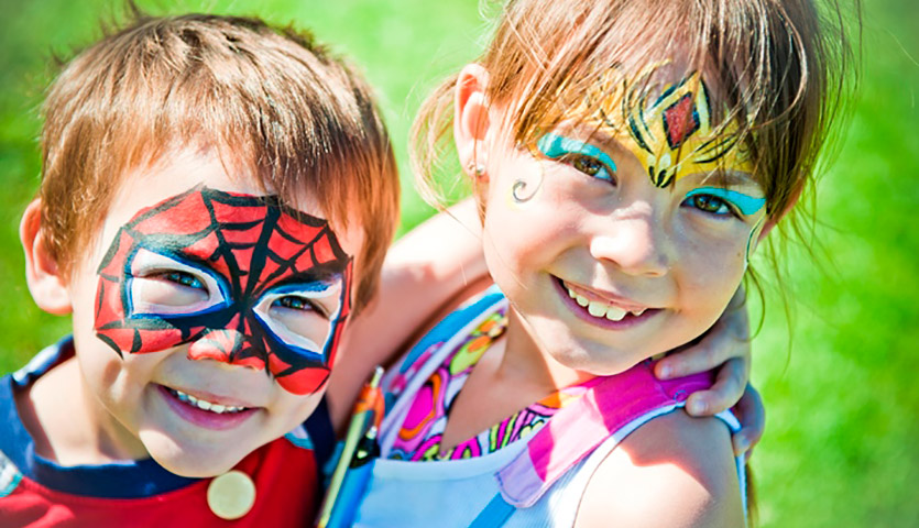A young boy with his face painted like Spiderman, and a young girl with patterns painted on her forehead.