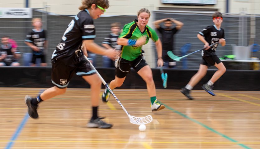 Three people playing floorball, an indoor hockey-like game.