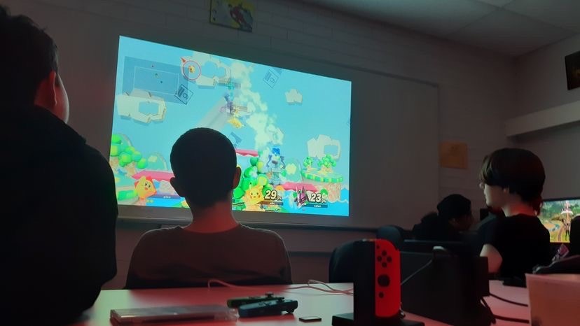 Three teenagers with their backs to camera, in a dark room playing Mario.