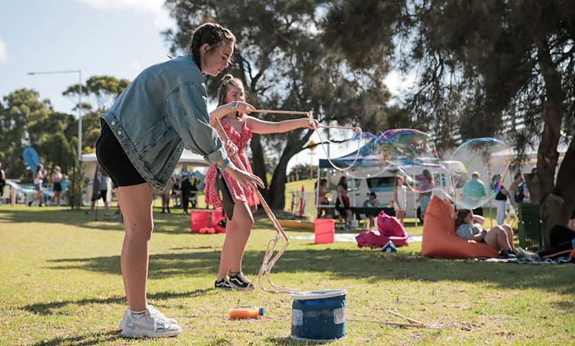 Two teenage girls in a park playing with bubble wands.