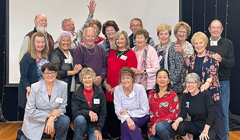 A group of 16 senior citizens from a glee club gathered in front of a blank screen.