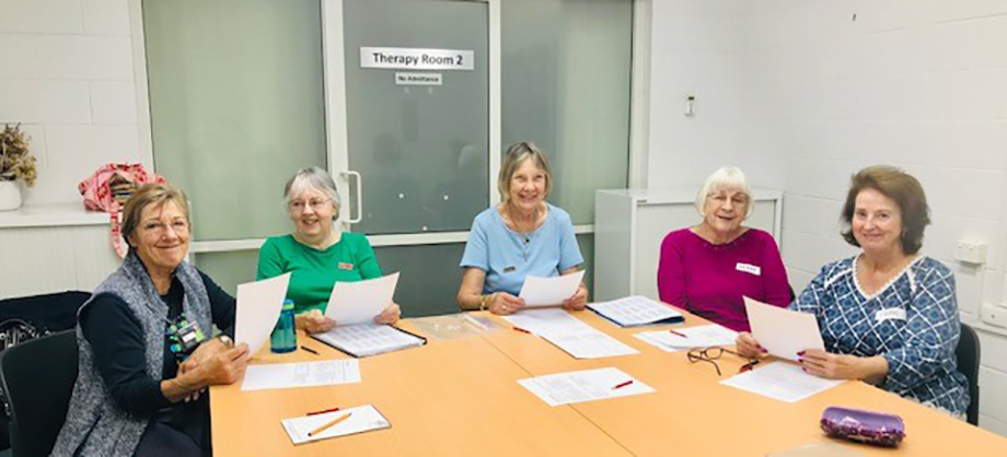 Five people sitting at a table smiling and holding a piece of paper each.