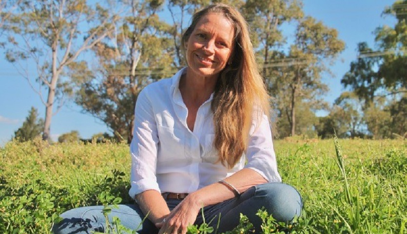 Author Portland Jones wearing blue Jeans and a white shirt sat in a field of grass with trees as a backdrop.