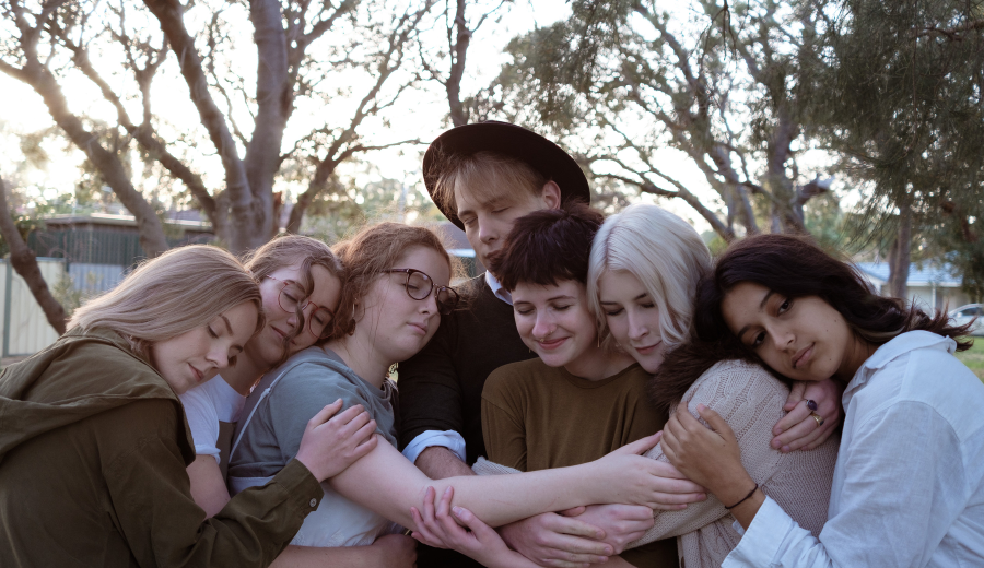 Seven young performers hugging in a group embrace