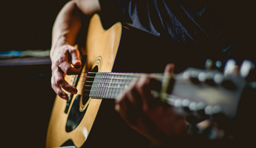 Close-up of a hand strumming the strings of a light brown guitar