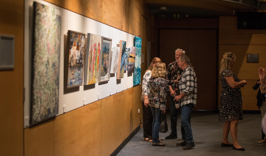 Small gathering of friends stood admiring artwork in a dimly lit art exhibition