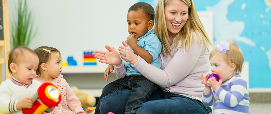 A lady clapping her hands and smiling with four babies around her