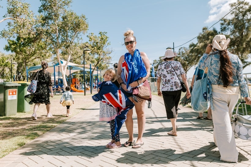 Lady and child draped in an Australia flag on the Eastern Foreshore as people walk past