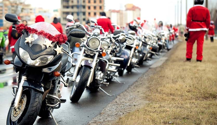 A line of parked motorcycles with Christmas decorations and riders in the background wearing Santa costumes