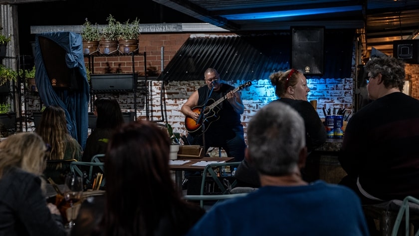 Male acoustic musician playing live in a bar with people sitting and listening.