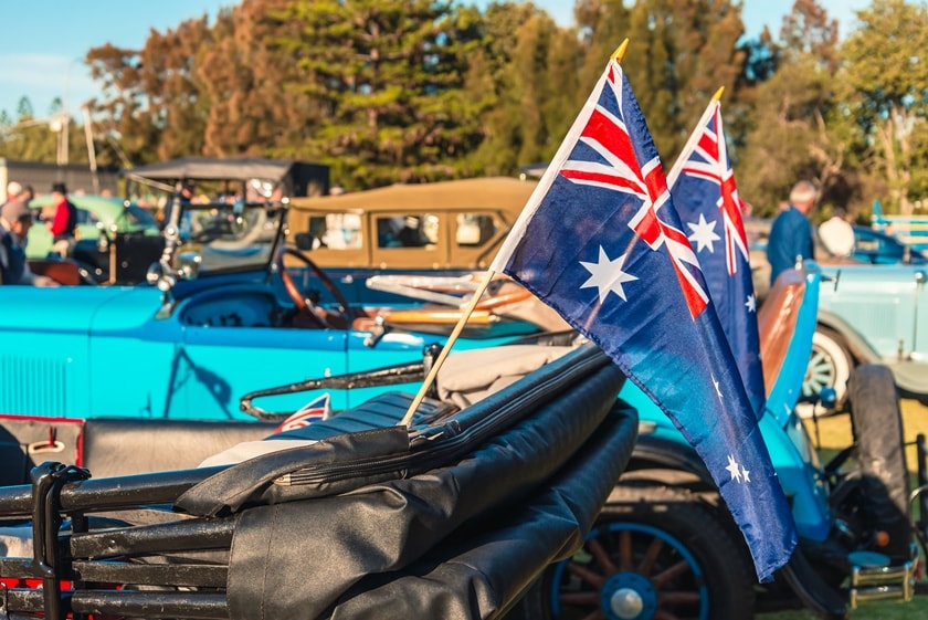Two Australian flags on the back of a vintage car with the top down. Other vintage cars in the background.