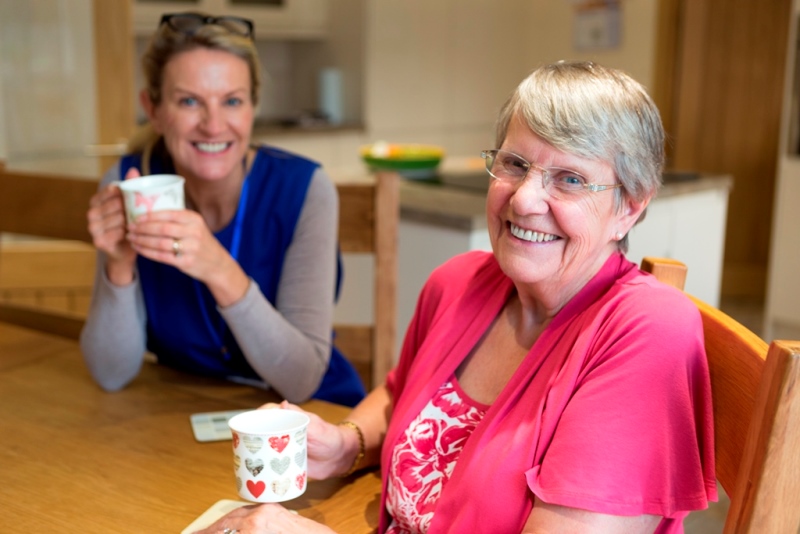 Care worker joins an an elderly woman for a cup of tea