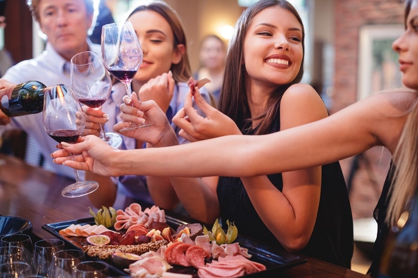 3 happy women sitting at a bar with a savoury meat platter and drinking red wine.