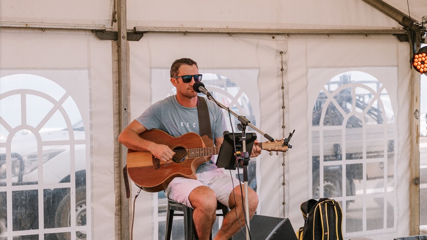 Male musician playing an acoustic guitar sitting in front of a mic in a marquee