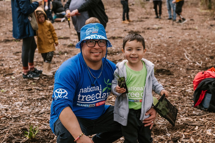 Man and child holding a small plant wearing National Tree Day shirts and hats.