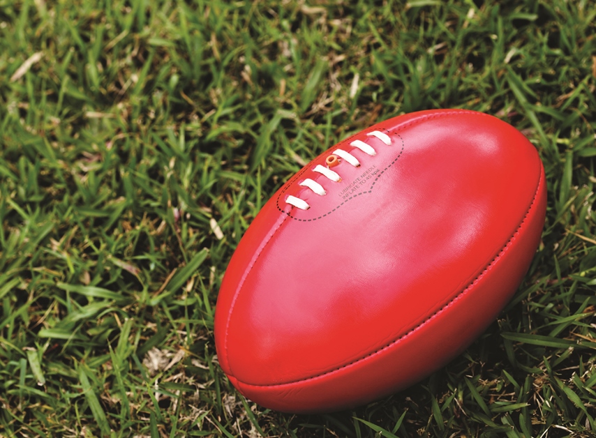 A red AFL football lying on the grass