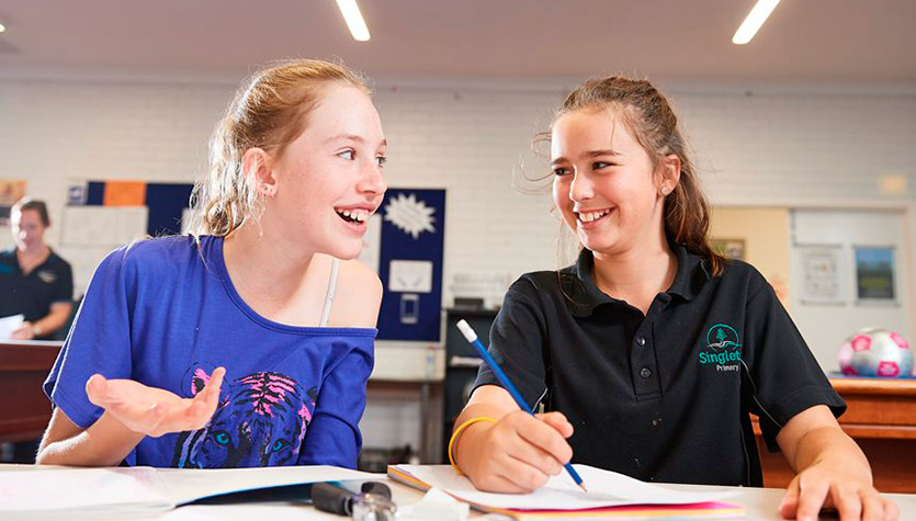 Two teenage girls talking and writing at a desk