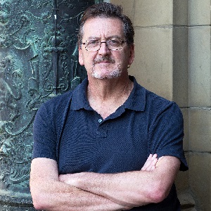 Author Alan Carter wearing a blue polo shirts stood in front of an ornate iron door