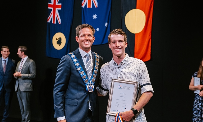 Mayor Rhys Williams with Citizen of the Year Award youth winner Liam Gould standing in front of flags