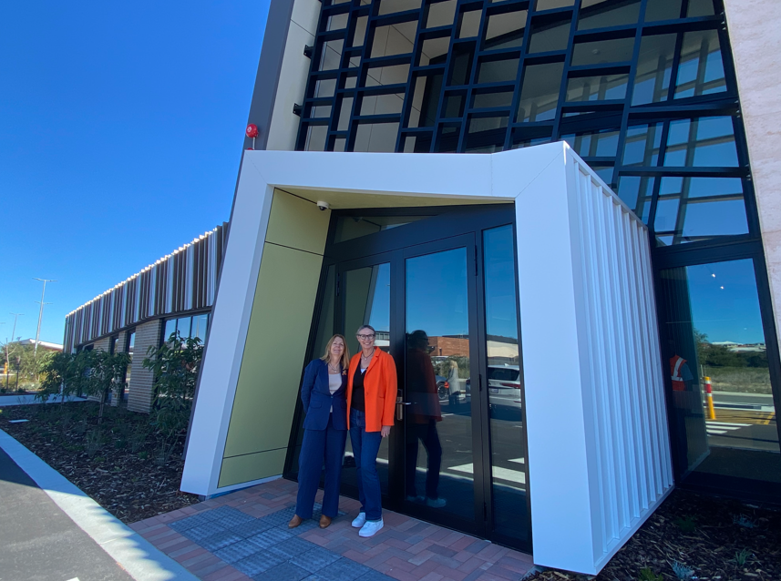 Two women stand side by side and smile for camera outside the community centre