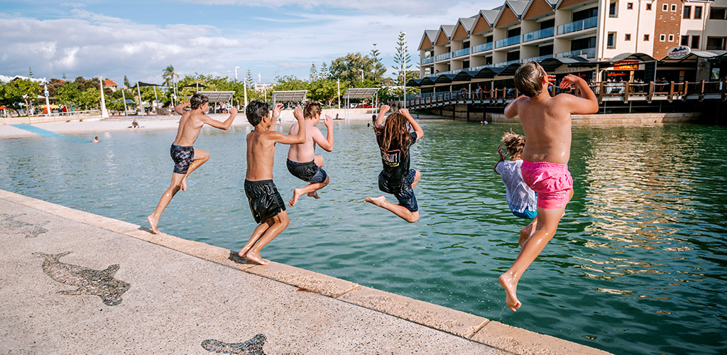 Six kids are jumping from a platform into the water in Mandurah