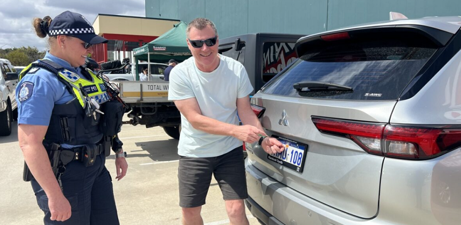 Police officer with a member of the community changing the screws on a car license plate