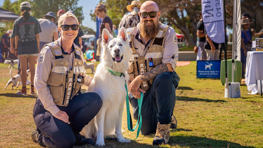 Two City of Mandurah Rangers kneeling down next to a dog on the grass