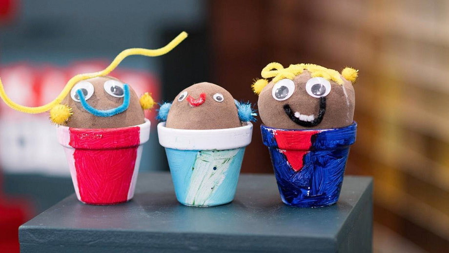 Three grass-head creations made by kids in little plant pots.