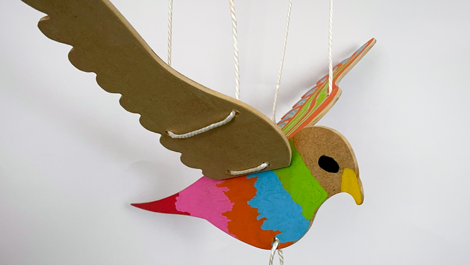 Filipino Wooden Bird Craft with colours painted on it, hanging by some string.