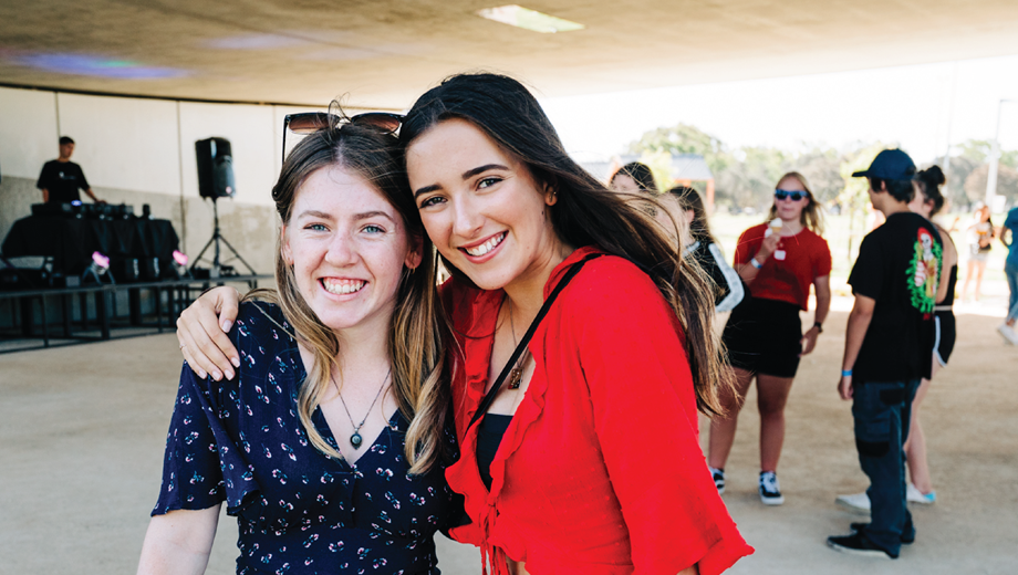 Two young ladies at a past Beats Under the Bridge event with their arms around each other smiling at the camera.